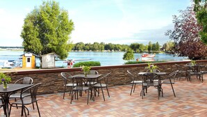 An outdoor patio with tables and chairs, a stone wall, and a view of a lake with boats.