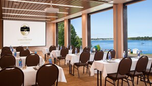A conference room with tables set for a meeting, large windows with a view of a lake, and a projection screen displaying 'The Lakefront Anchorage' logo.