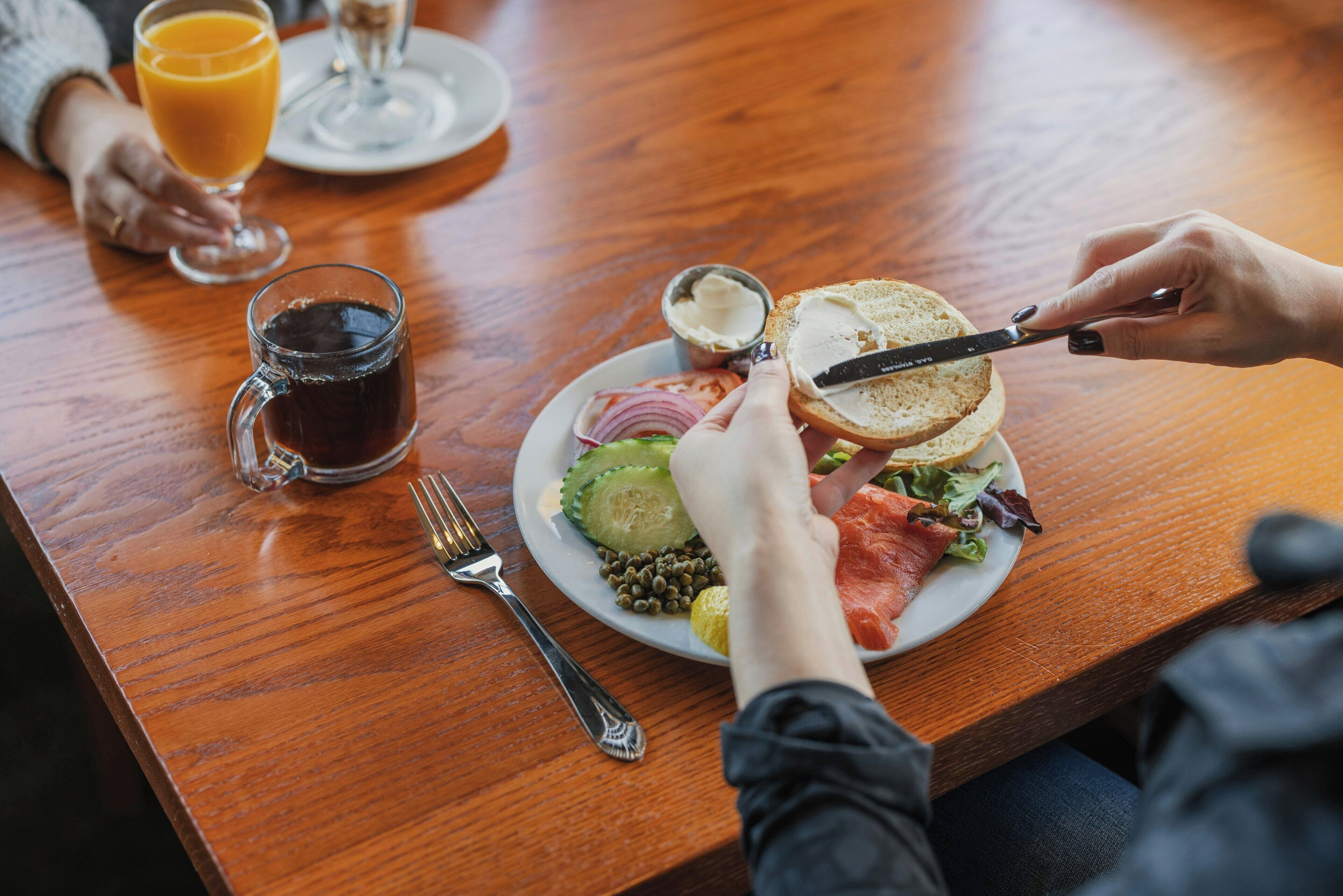 A wooden table with a plate of food, a glass of orange juice, and a glass of dark liquid.