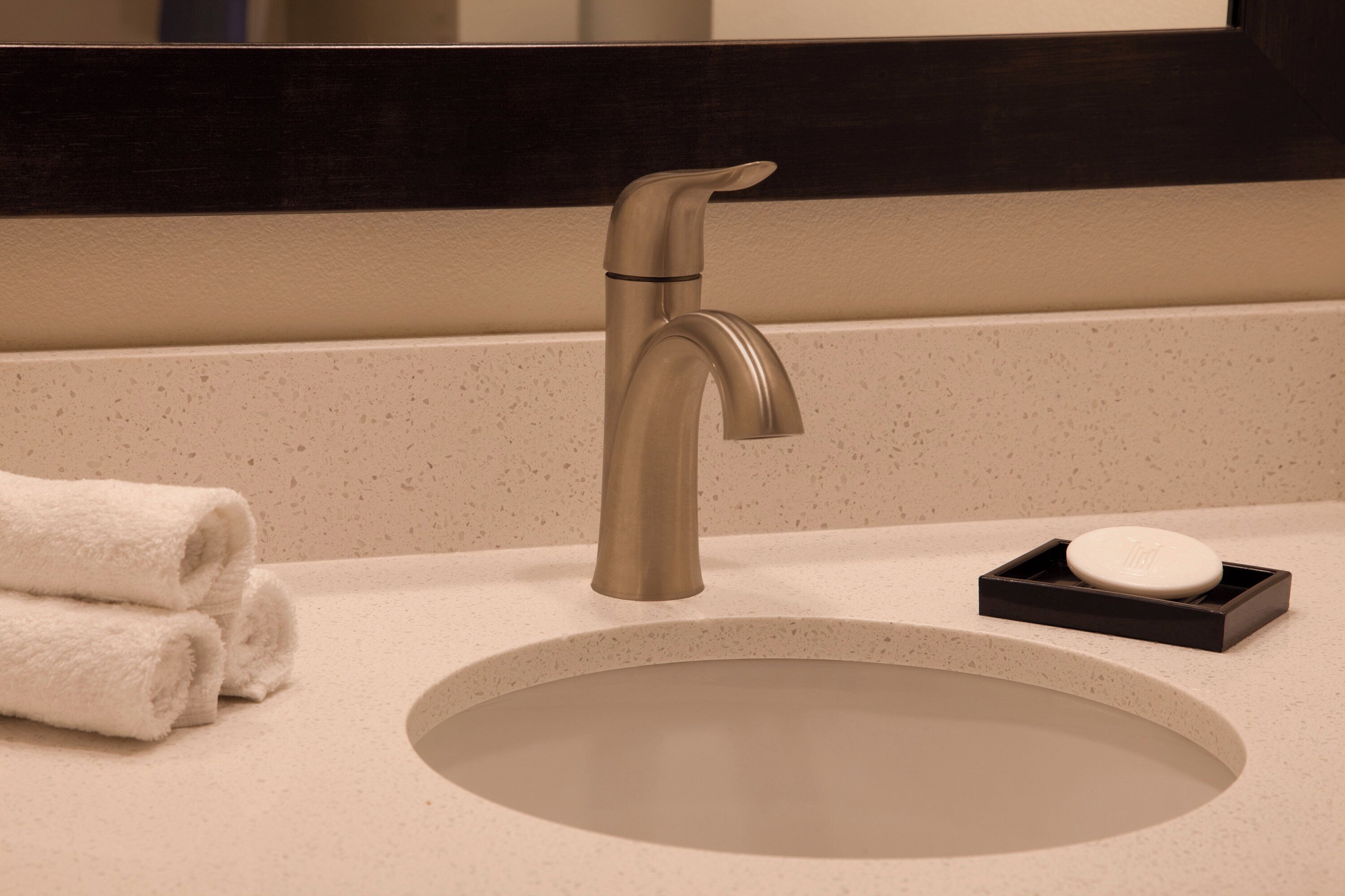 A bathroom sink with a modern faucet, a round mirror above it, and a soap dish with a bar of soap.