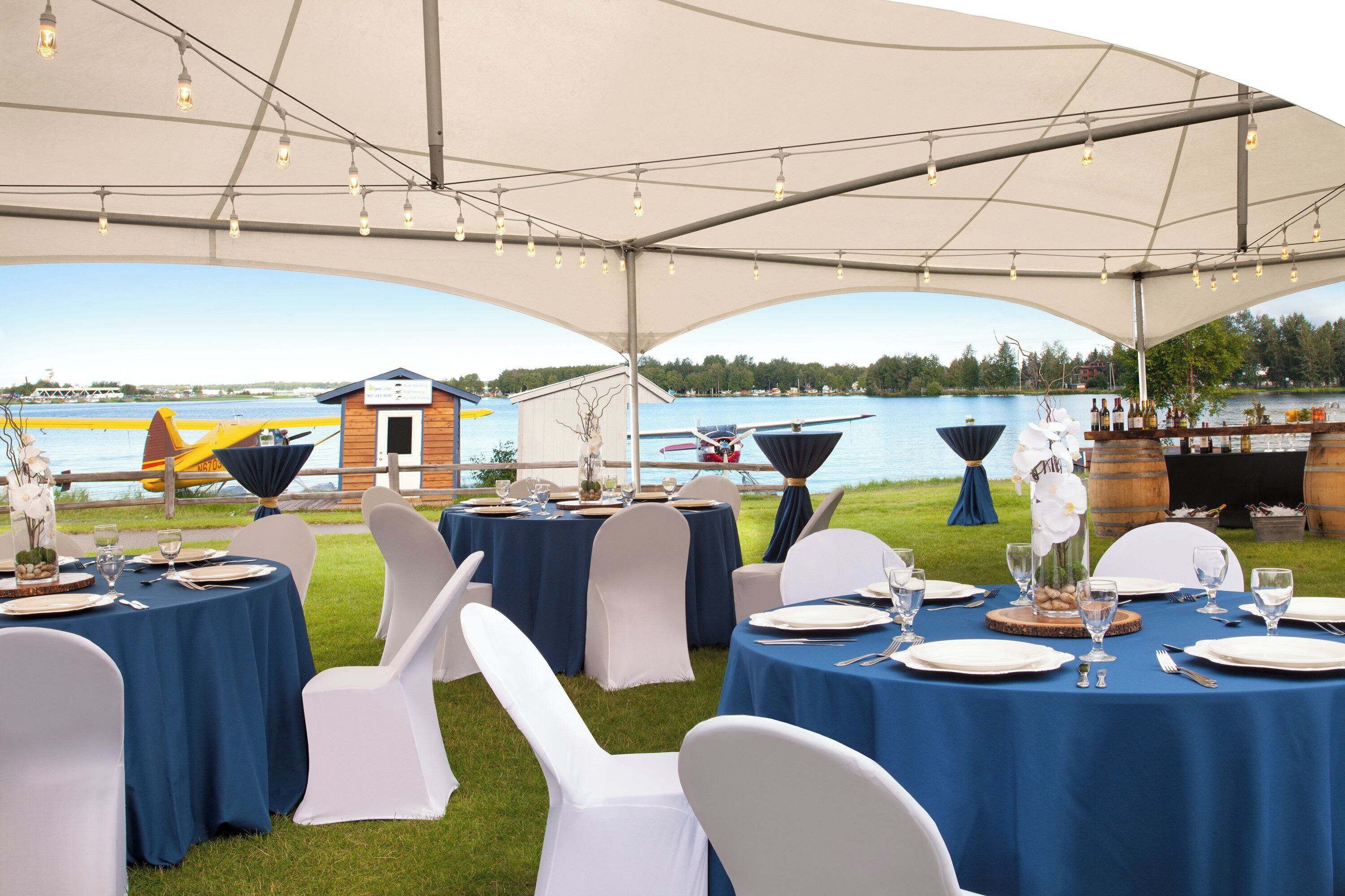 An outdoor dining area with tables set for a meal, overlooking a body of water and a dock.