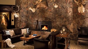 A stone wall with mounted animal heads, a fireplace, leather furniture, and a patterned carpet.