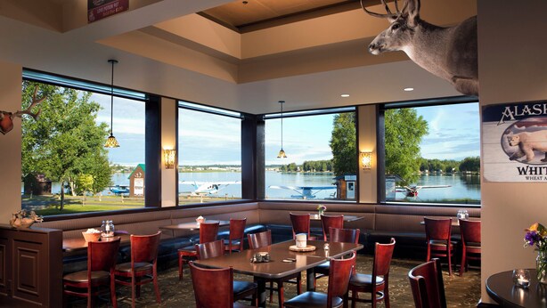 A restaurant with a view of a lake, wooden furniture, and a mounted deer head.