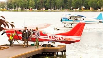 Un petit avion rouge est garé sur un quai en bois, au bord d’un lac, avec d’autres avions en arrière-plan.