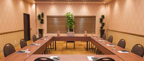 A conference room with a long table, chairs, potted plants, and a laptop.