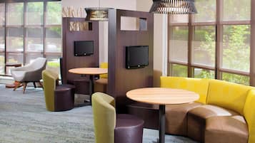 A modern lounge area with a curved yellow sofa, round tables, and a TV mounted on a wooden partition.