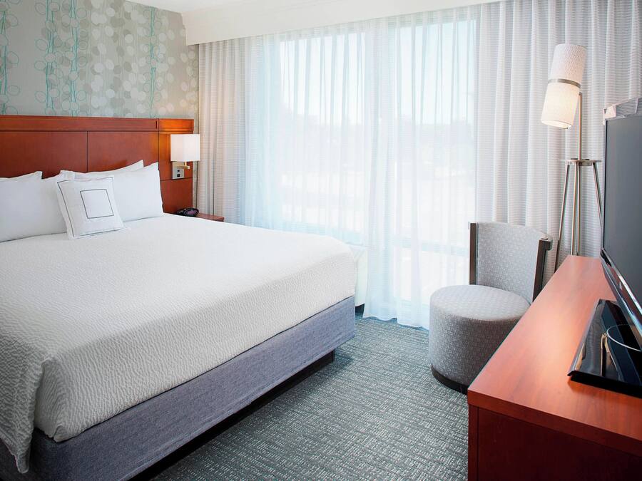 Una habitación de hotel con una cama grande, televisión, escritorio y una silla.