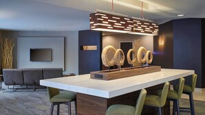 A modern kitchen with a large island, bar stools, a flat-screen TV, and decorative wooden rings. - Courtyard By Marriott Ann Arbor (Ann Arbor)
