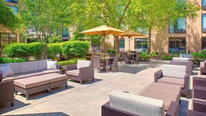 An outdoor patio with wicker furniture, including sofas and chairs, and a table with an umbrella. - Courtyard By Marriott Ann Arbor (Ann Arbor)