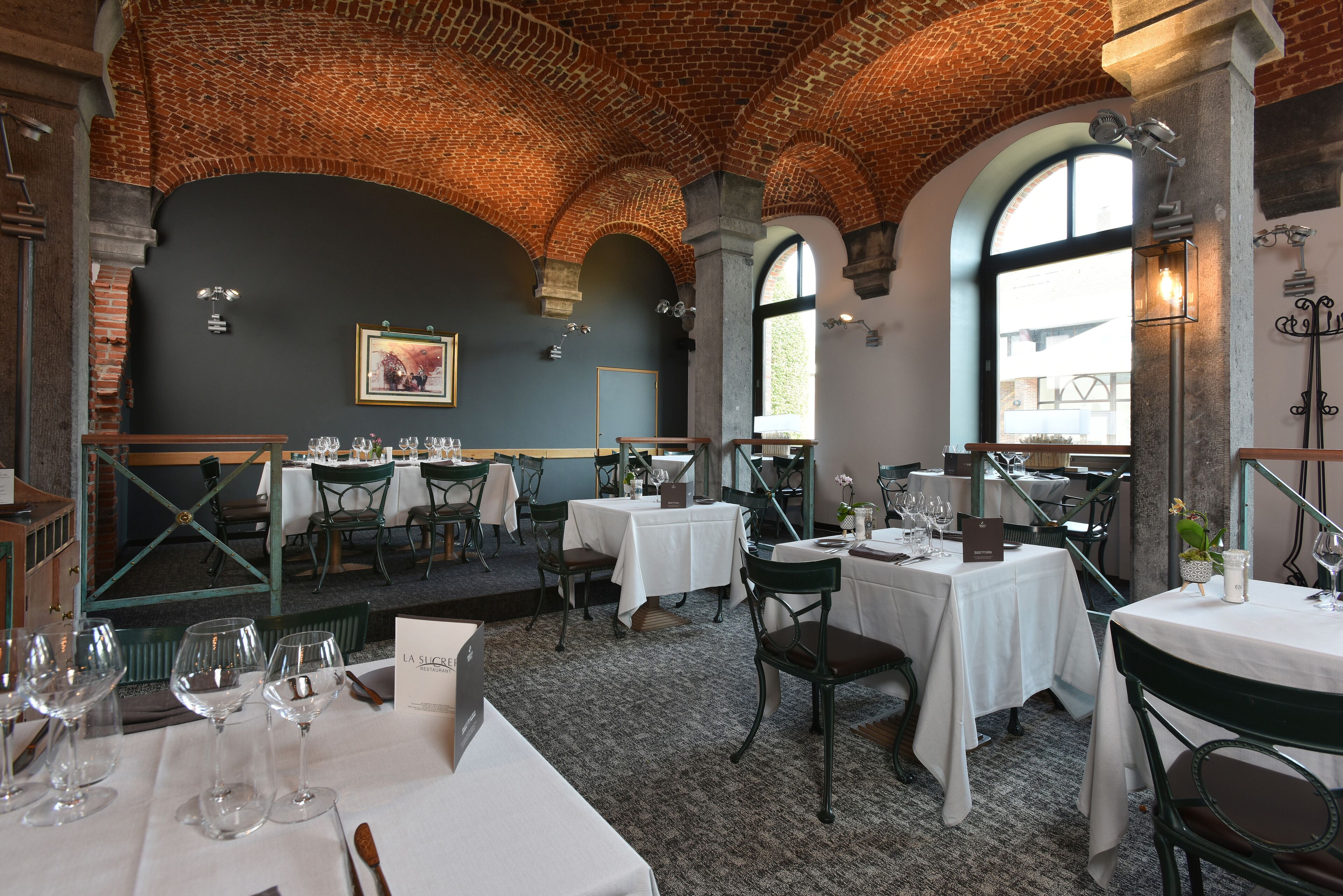 Um restaurante com arcos de tijolo, mesas e cadeiras brancas.