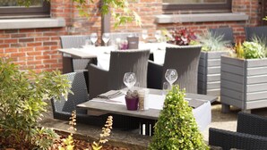 An outdoor dining area with wicker furniture, a brick wall, and potted plants. - Van der Valk Waterloo (Waterloo)