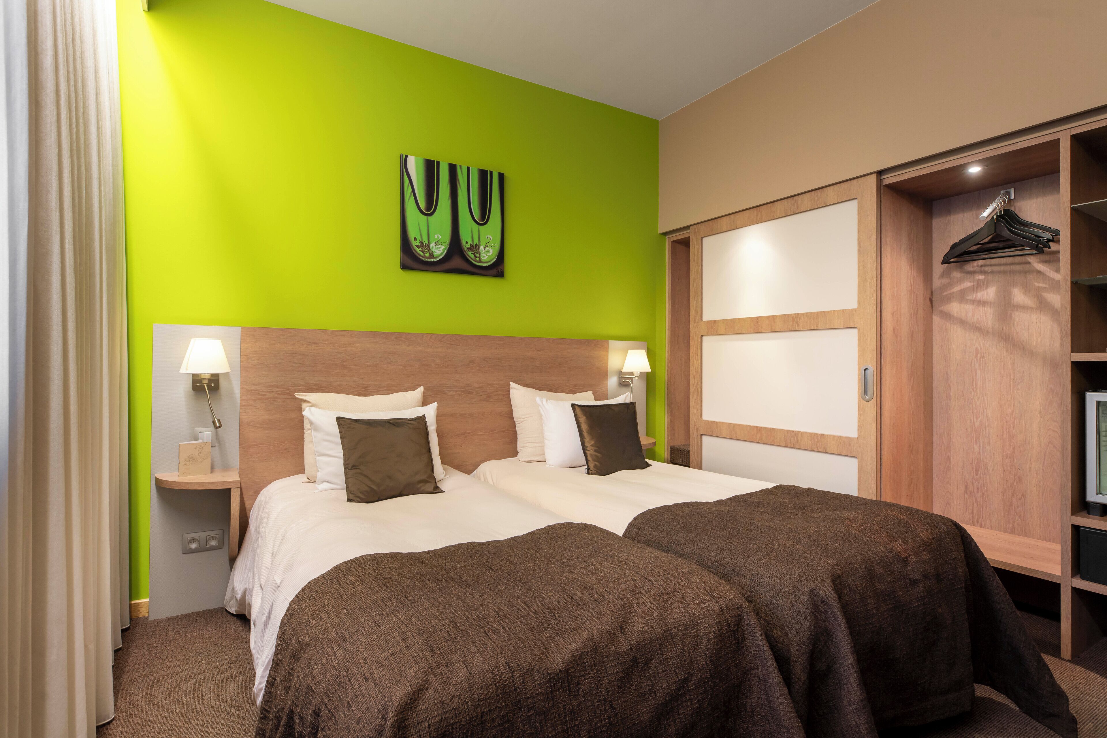 A hotel room with two beds, a green wall, a wooden headboard, a wardrobe, and a painting.
