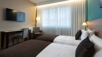 Hotelkamer met twee bedden, een bureau, een stoel, een televisie en een raam met gordijnen.