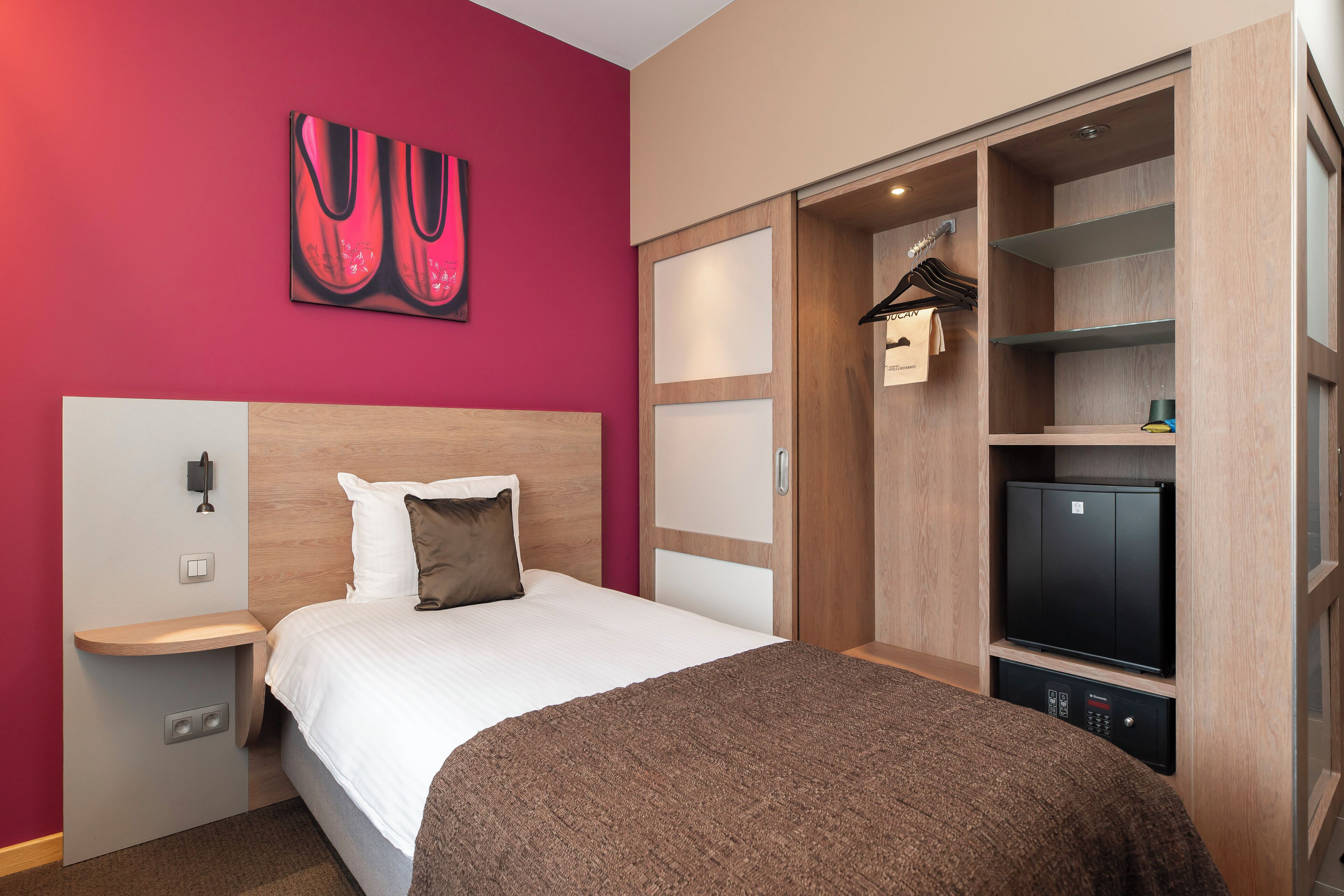 A hotel room with a bed, a wardrobe, a television, and a painting on the wall.