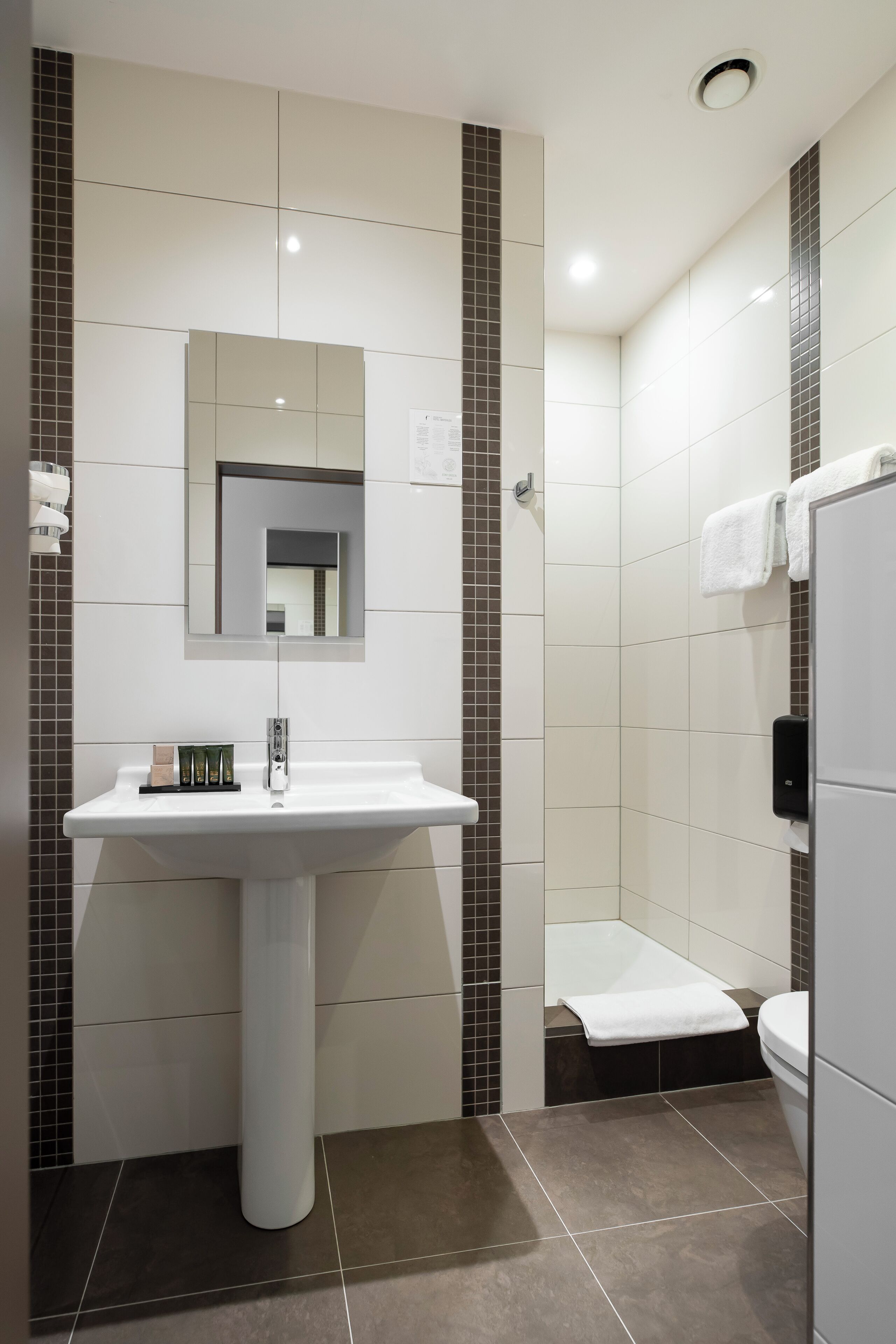 Un baño moderno con lavamanos pedestal, espejo y retrete.