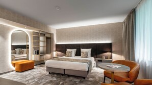 A modern hotel room with a large bed, a seating area with a round table, and a built-in shelving unit. - Van der Valk Waterloo (Waterloo)