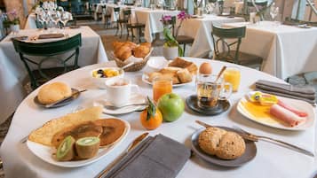 Une table dressée pour le petit-déjeuner, avec divers plats, notamment des croissants, des fruits et des pâtisseries, disposés dans un coin repas.