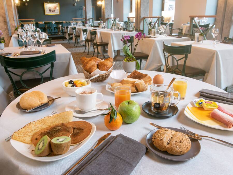 Une table dressée pour le petit-déjeuner, avec divers plats, notamment des croissants, des fruits et des pâtisseries, disposés dans un coin repas.
