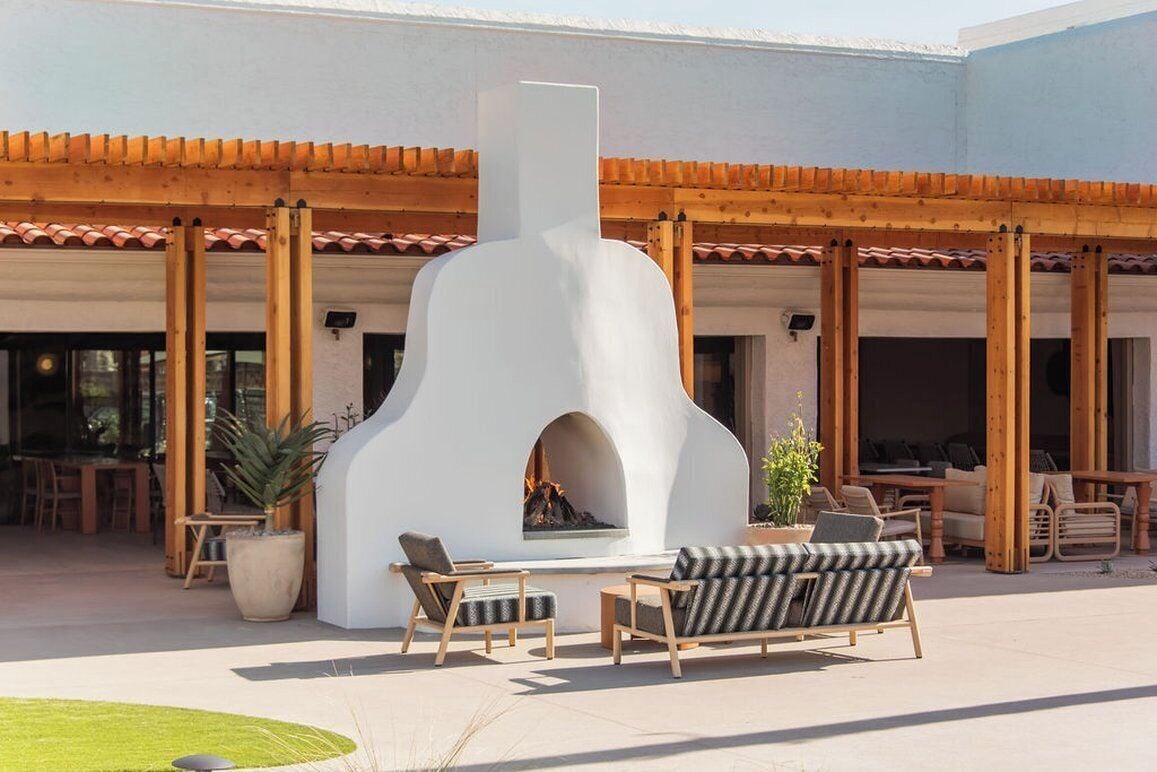 Une terrasse extérieure dotée d’une cheminée en pierre, de meubles en bois et d’une structure en forme de pergola.