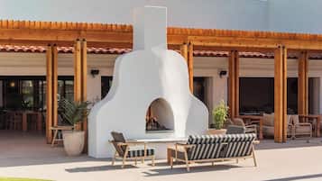 An outdoor patio with a stone fireplace, wooden furniture, and a pergola structure.