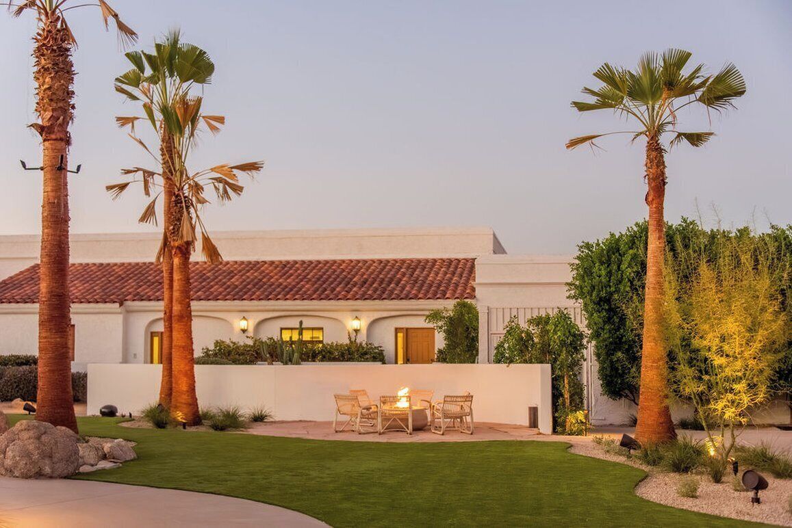 A house with a patio, palm trees, and a fire pit.