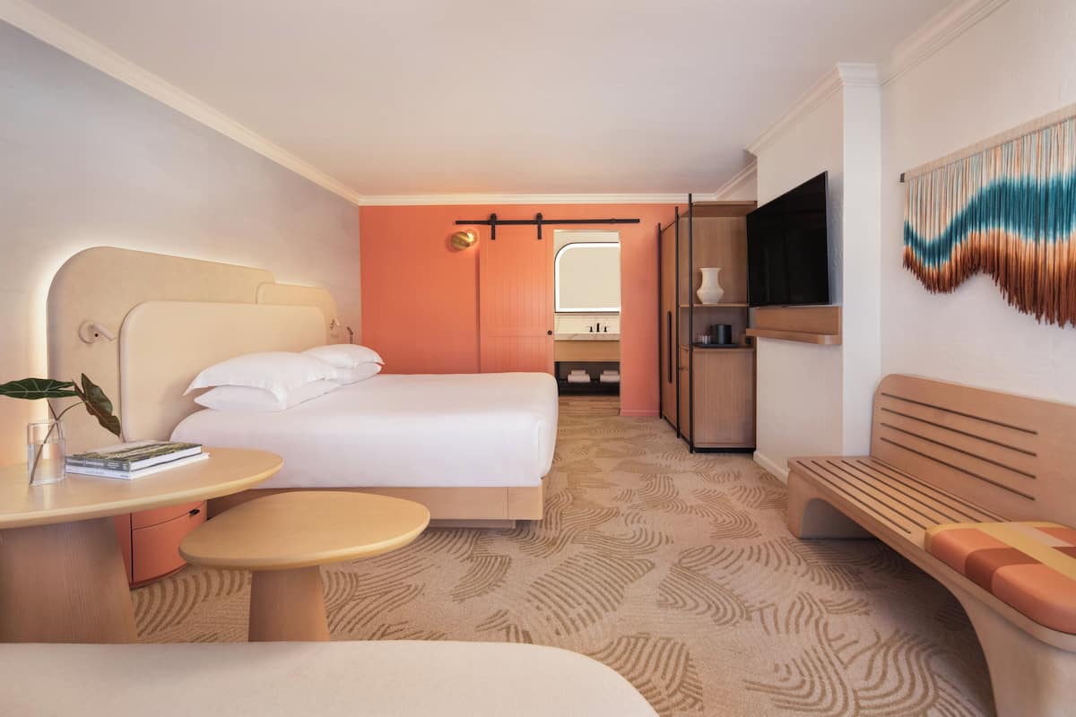 Habitació d'hotel amb un llit, escriptori, banqueta, televisió i un bany visible a través d'una porta oberta.