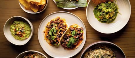 Variedad de platillos, como tacos, guacamole y totopos, sobre una mesa de madera.