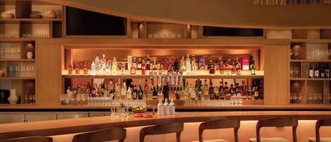 A bar area with multiple liquor bottles, glasses, and wooden chairs.