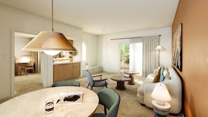 Ein modernes Hotelzimmer mit Essbereich, einer Sofagarnitur und einer durch eine offene Tür einsehbarer Küche.
