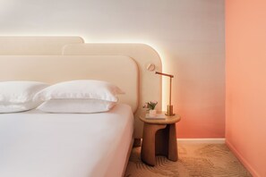 Un lit bien fait, avec du linge de lit blanc et des oreillers, une table de chevet avec une lampe et une petite plante.