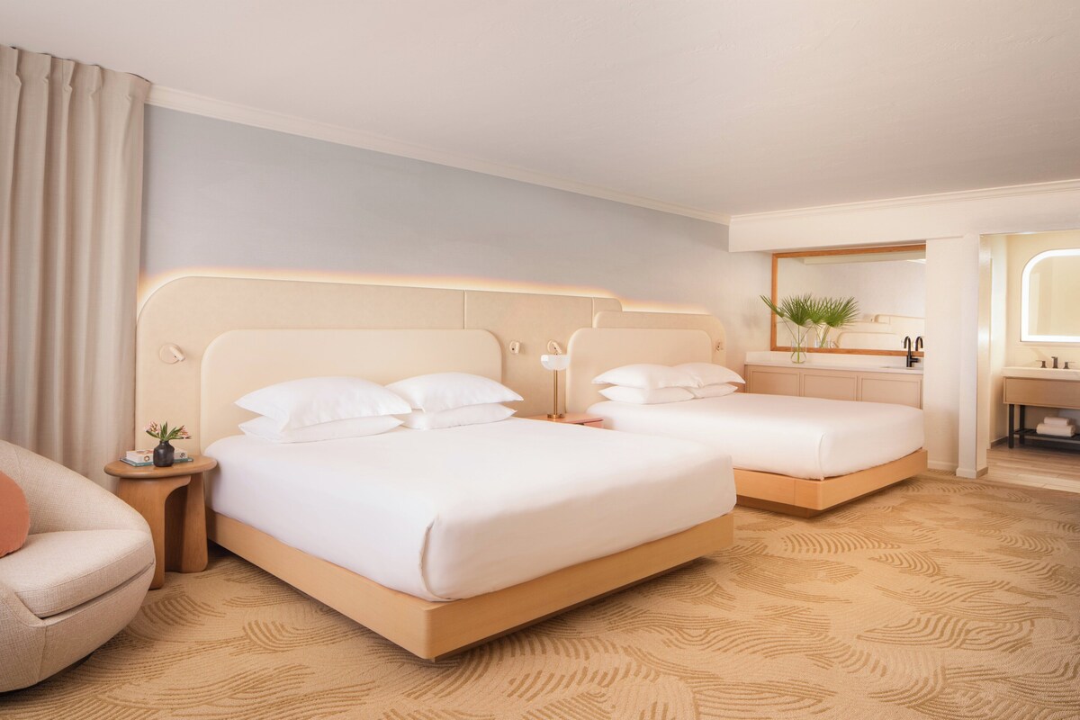 Une chambre d’hôtel avec deux lits, un coin salon, une salle de bain et un grand miroir.