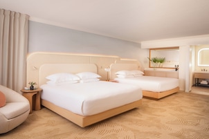 Quarto de hotel com duas camas, área de estar, banheiro e um espelho grande.
