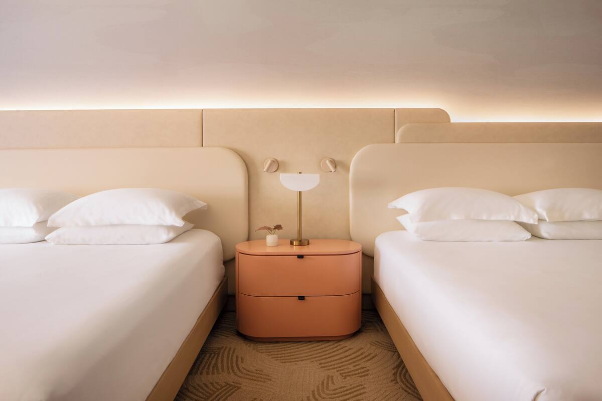 Habitación de hotel con dos camas, una mesita de noche con lámpara y una planta pequeña.