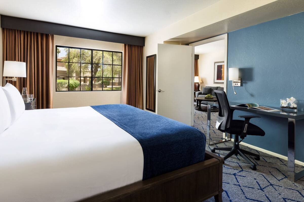 Ein Hotelzimmer mit einem großen Bett, einem Schreibtisch, einem Sessel und Blick ins Freie.