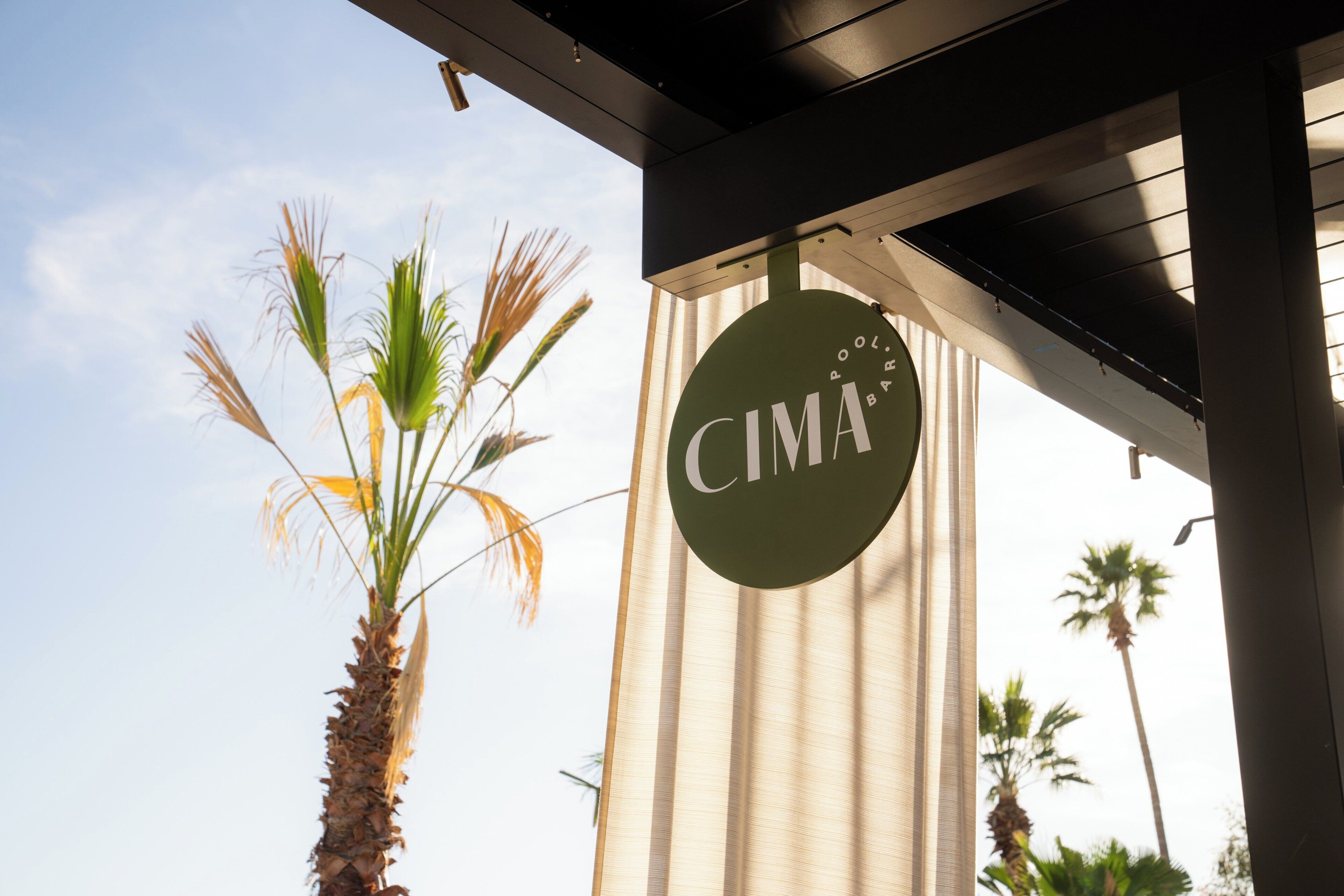 Eine Palme, ein Gebäude mit dem Schriftzug 'CIMA' und ein klarer Himmel.
