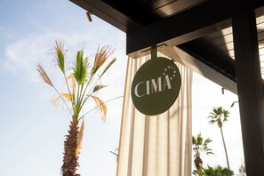 Un palmier, un bâtiment sur lequel on peut lire l’inscription « CIMA », et un ciel dégagé.