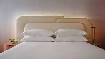 A neatly made bed with white linens and pillows, a bedside plant, and a modern lamp on a bedside table.