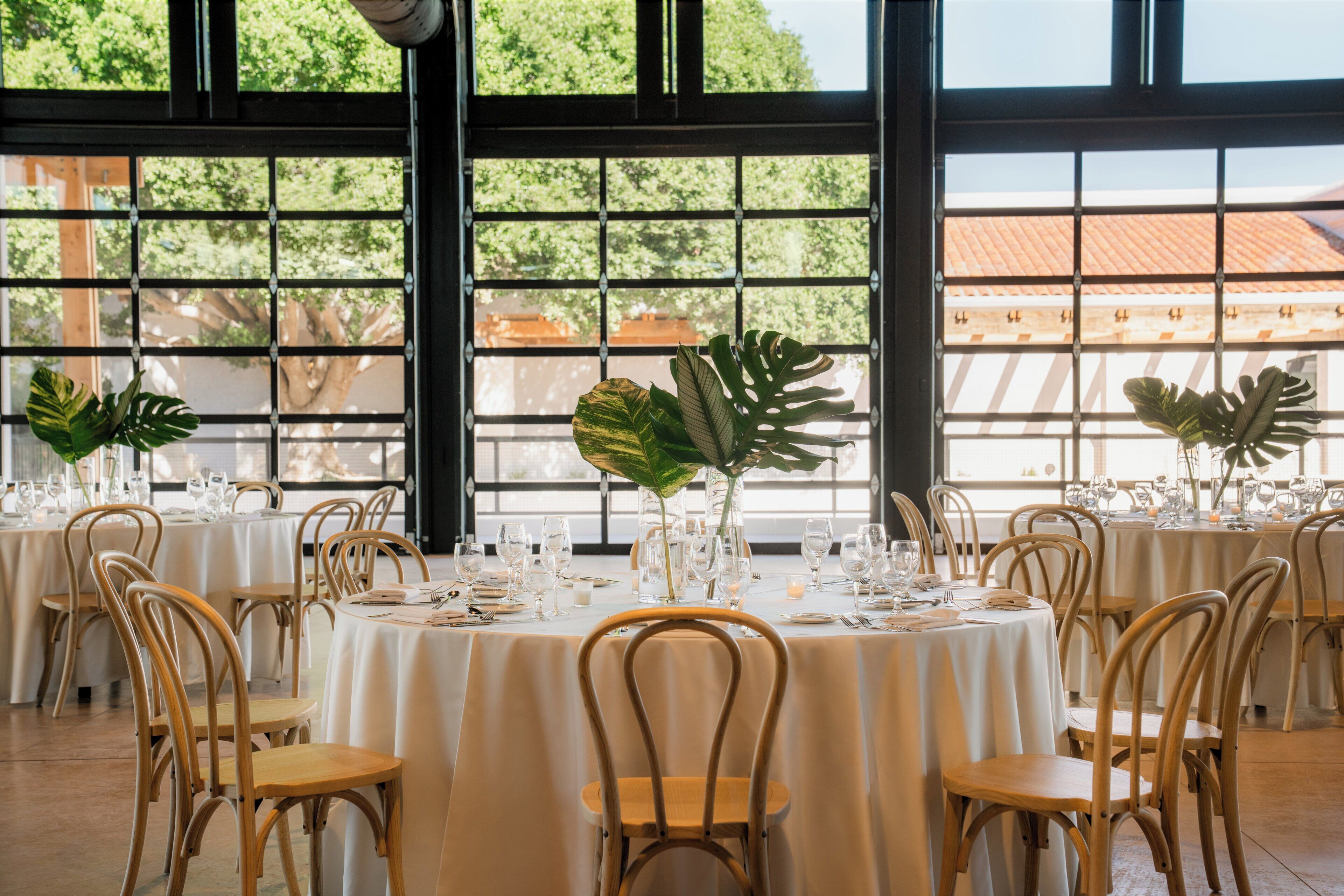 A dining area with round tables, chairs, and large windows with a view of buildings and trees.