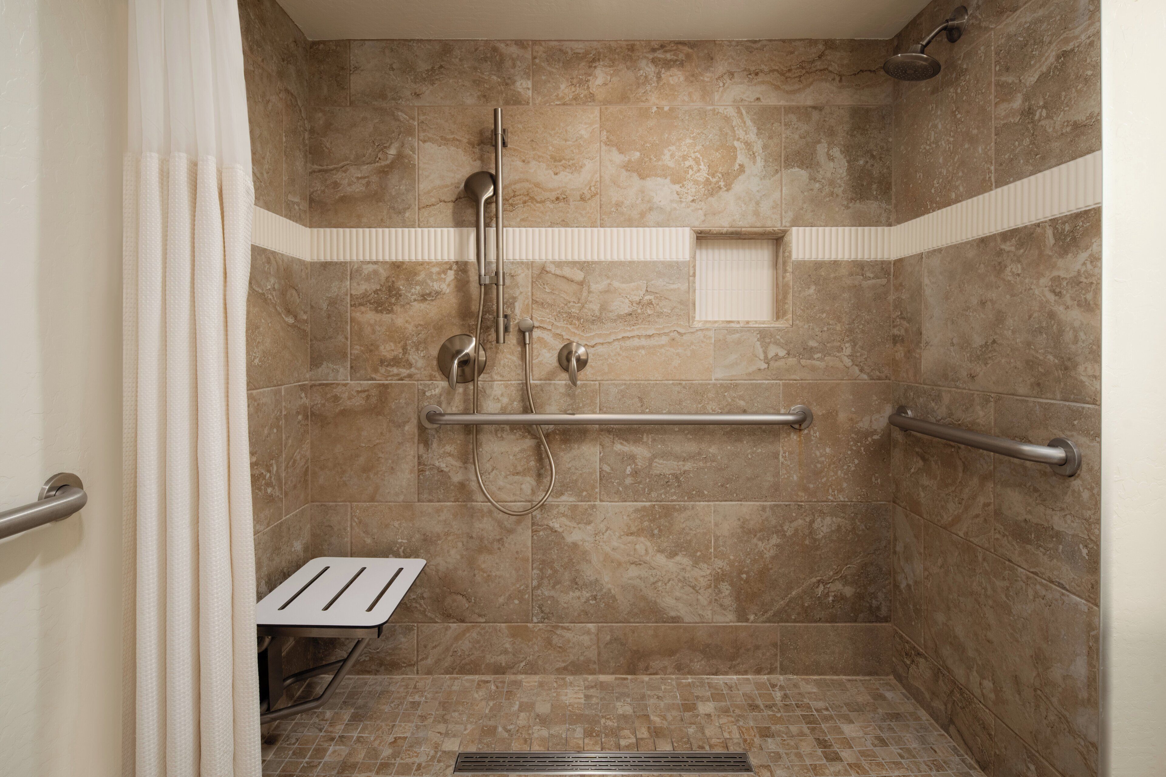 Eine ebenerdige Dusche mit Handläufe, Duschkopf und Bedienfeld.