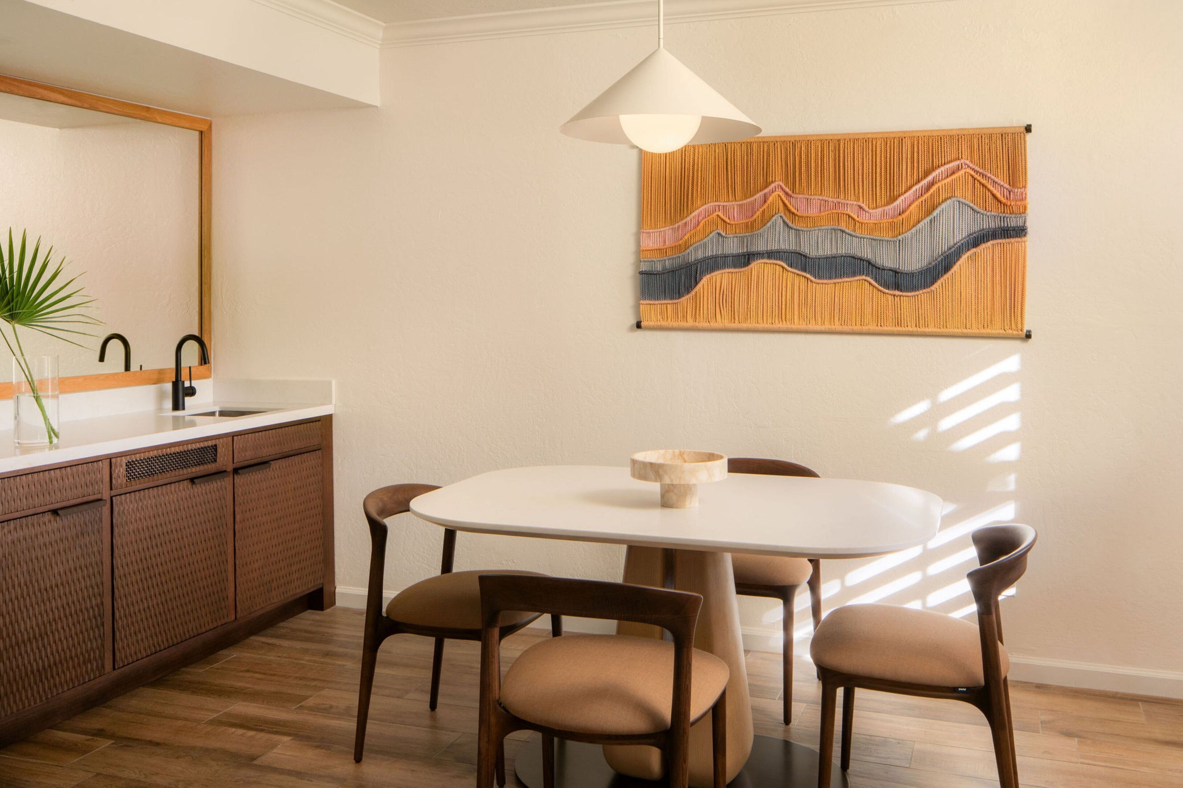 Una cocina moderna con encimera blanca, armarios de madera y un comedor con mesa redonda y cuatro sillas.