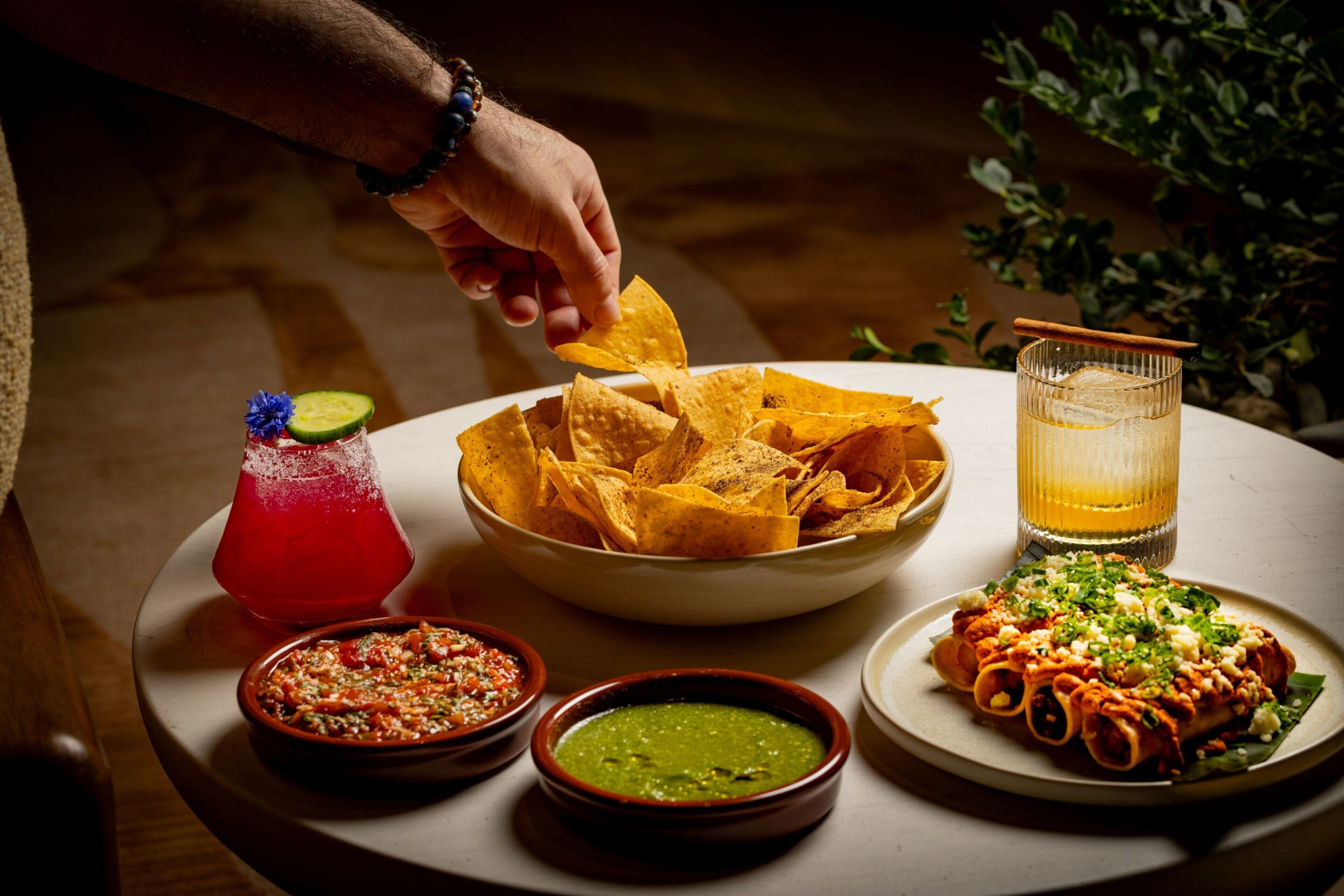 A table with nachos, a drink, and two bowls of dips.