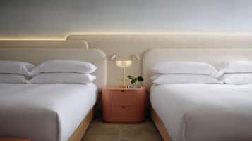 Quarto de hotel com duas camas, uma mesa de cabeceira com abajur e uma pequena planta.