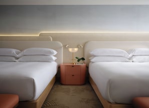 Een hotelkamer met twee bedden, een nachtkastje met een lamp en een kleine plant.