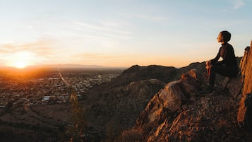 A person sitting on a rocky outcrop overlooking a cityscape during sunset.