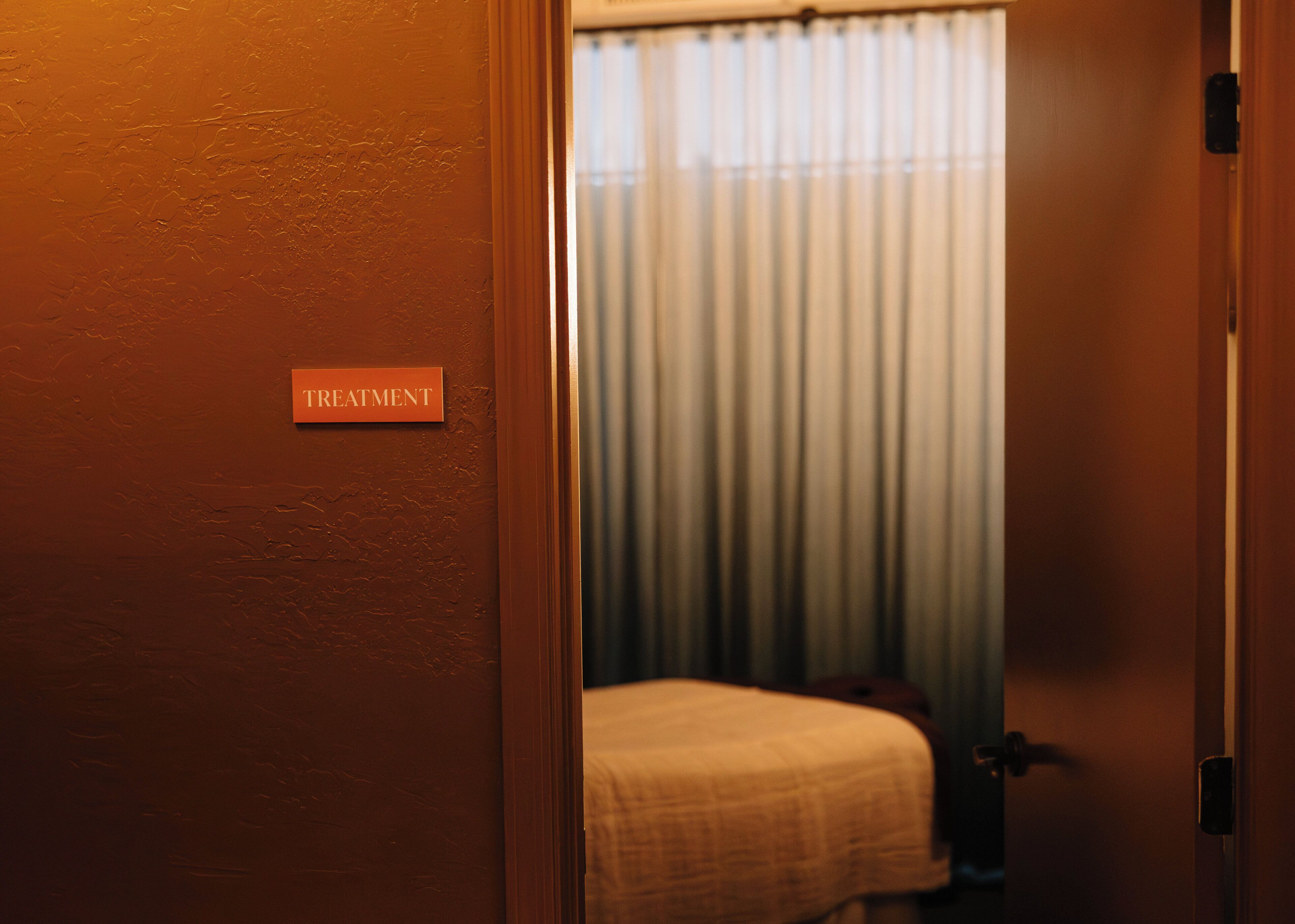 A room with a bed, a door labeled "TREATMENT", and a window with curtains.