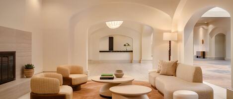 A spacious lobby with a modern design, featuring a sofa, armchairs, a coffee table, and a fireplace.