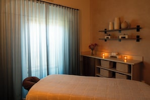 A bedroom with a bed, a nightstand, a wall-mounted shelf with decorative items, and sheer curtains. - Kimpton Miralina Resort & Villas by IHG (Paradise Valley)