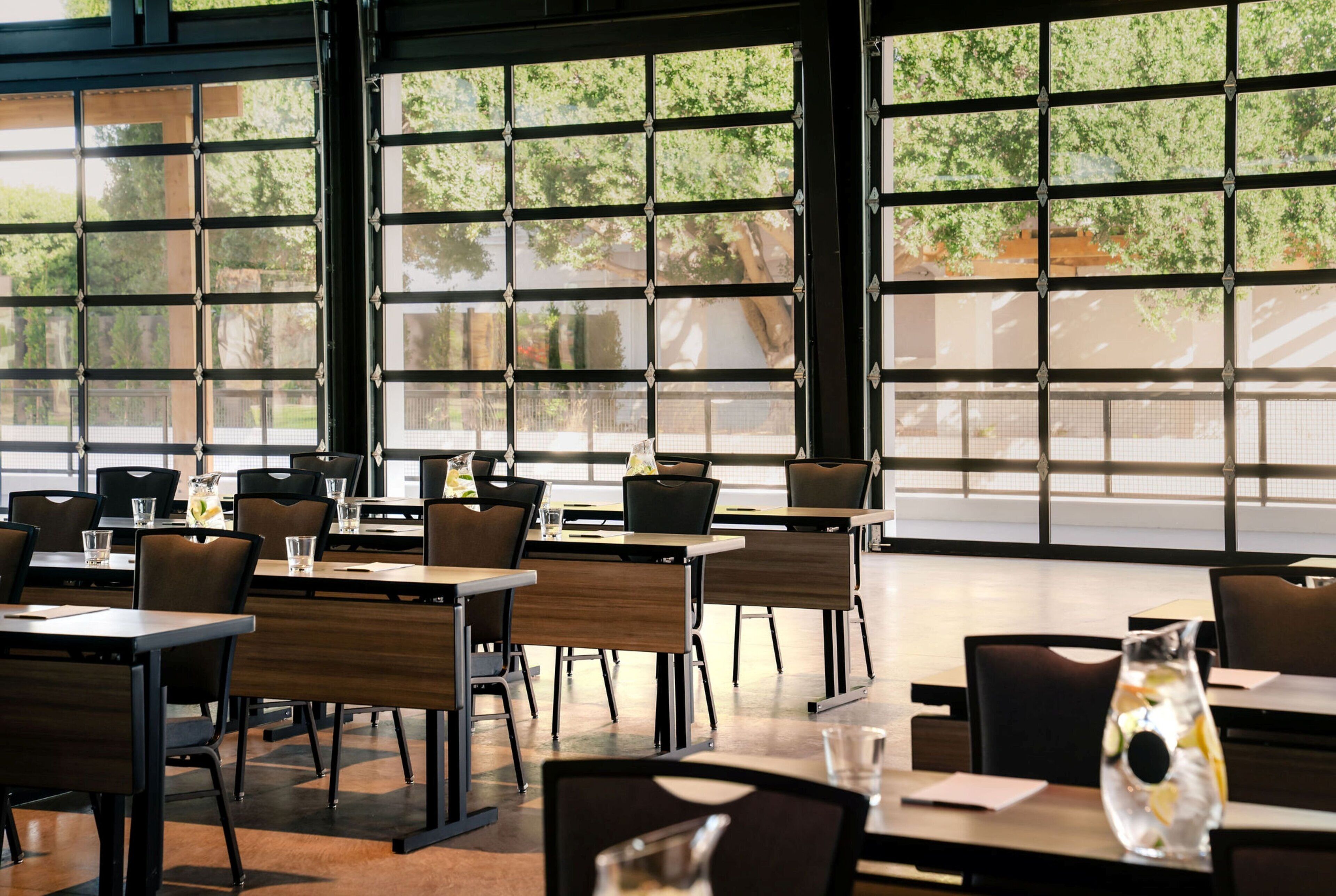 A restaurant with tables and chairs, large windows, and a view of trees and buildings.