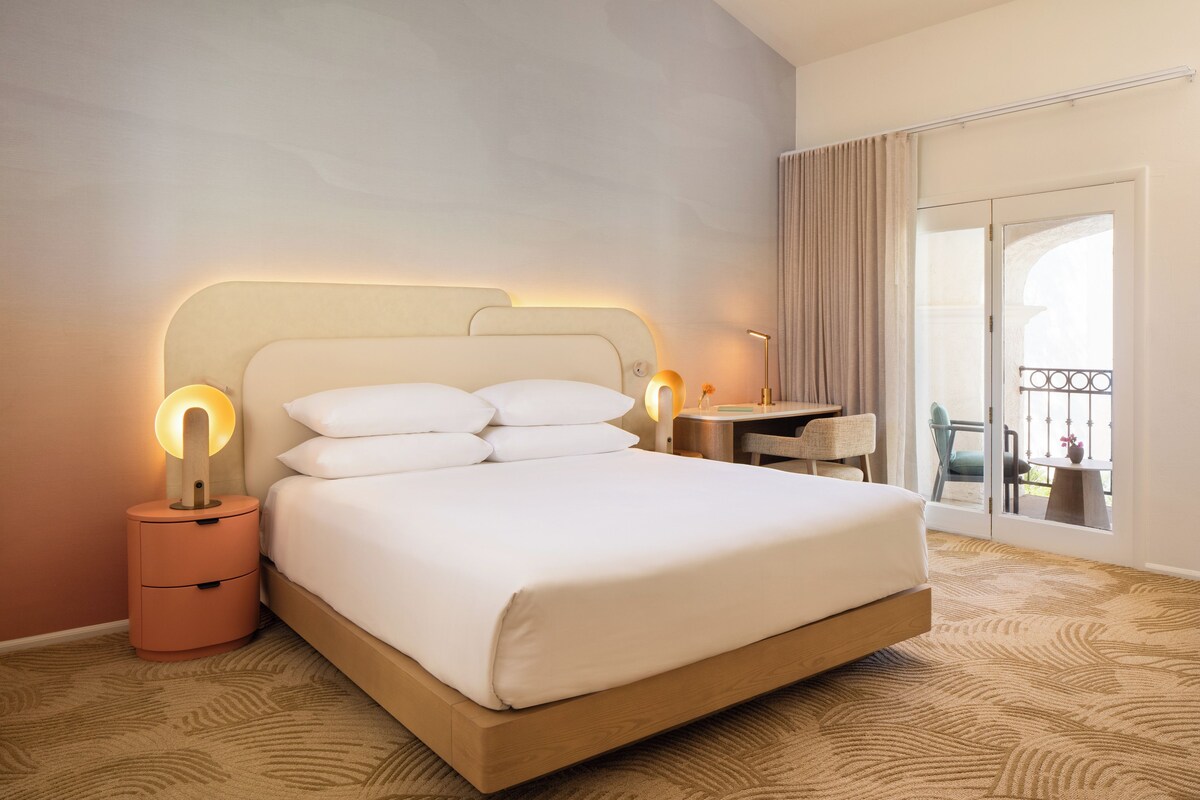 A hotel room with a large bed, bedside lamps, a desk, and a view of the outdoors.