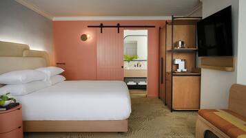 A hotel room with a large bed, a television mounted on the wall, a small seating area, and a bathroom visible through an open door.